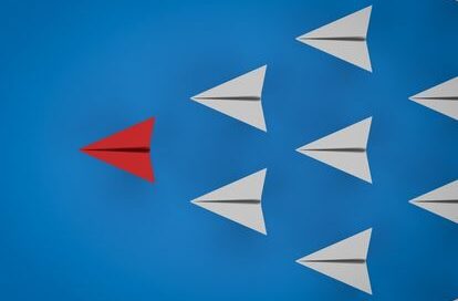 red paper plane leading the white paper planes